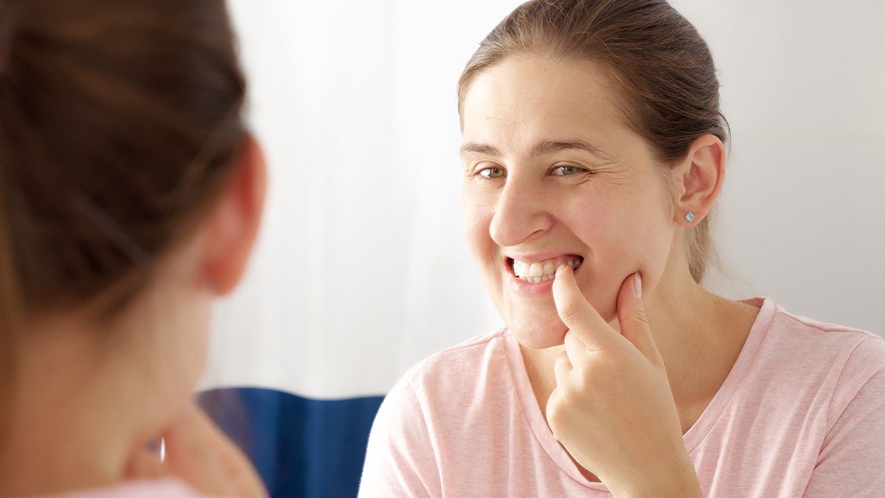 A woman check white stuff on her teeth in front of mirror.